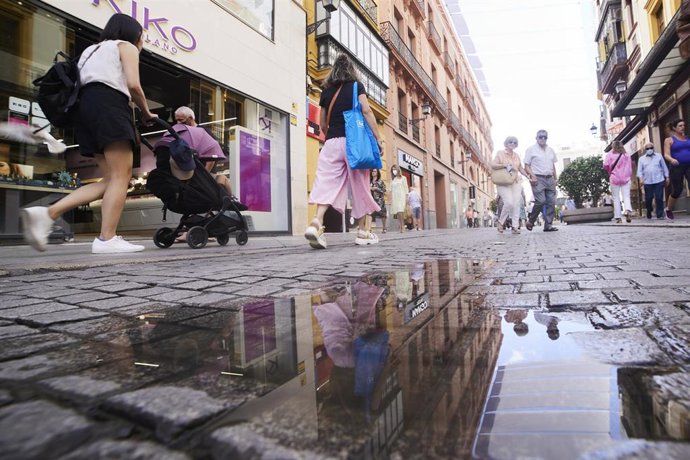 Archivo - Varias personas caminan y se reflejan en un charco en el suelo, en Sevilla. (Imagen de archivo).