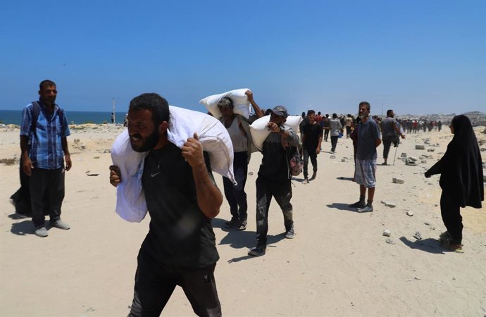 22 de julho de 2025, Gaza, Faixa de Gaza, Território Palestino: Pessoas caminham pela rua al-Rashid, no oeste de Jabalia, em 22 de julho de 2025, em direção a caminhões que transportam ajuda humanitária, depois de entrarem no norte da Faixa de Gaza atravé