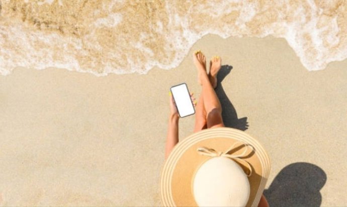 Mujer tomando el sol en la orilla de la playa utilizando el móvil.