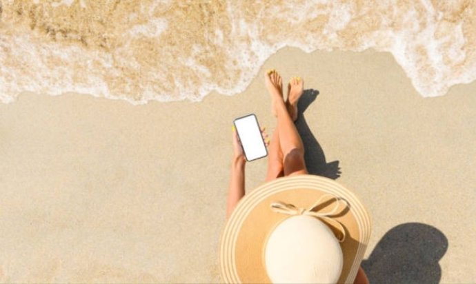 Mujer tomando el sol en la orilla de la playa utilizando el móvil.