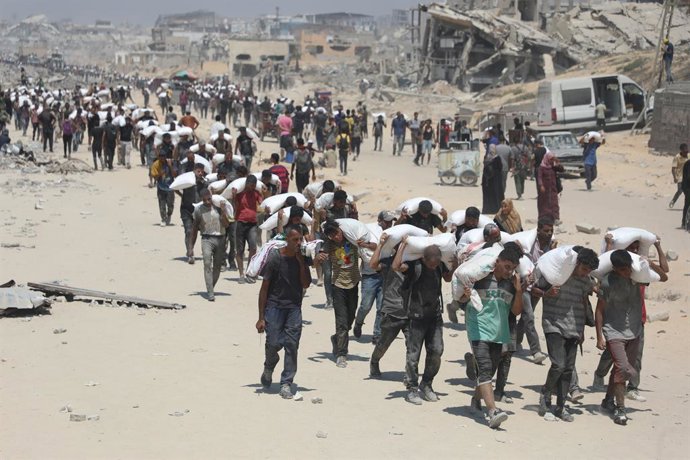27 de julho de 2025, Cidade de Gaza, Faixa de Gaza, Território Palestino: Pessoas caminham pela rua al-Rashid, no oeste de Jabalia, em direção a caminhões que transportam ajuda humanitária, depois de terem entrado no norte da Faixa de Gaza pela fronteira 