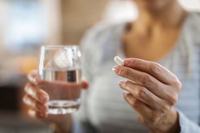 Archivo - Las manos de una mujer sostienen una píldora y un vaso de agua.