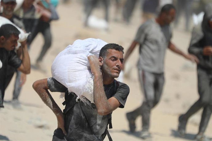 27 July 2025, Palestinian Territories, Gaza City: Palestinians carry sacks of flour from a humanitarian aid convoy, as they make their way along al-Rashid street. Against the backdrop of a looming hunger crisis in the Gaza Strip, large-scale aid deliverie