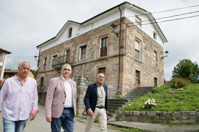 El consejero de Fomento, Roberto Media, con responsables del Ayuntamiento, en la fachada de las antiguas escuelas de Pesquera
