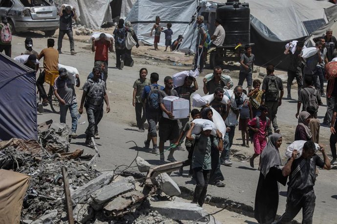 01 August 2025, Palestinian Territories, Jabalia: Palestinians carry sacks of flour they collected from a humanitarian aid convoy, as they make their way along a destroyed road in Jabalia.  Photo: Omar Ashtawy/APA Images via ZUMA Press Wire/dpa