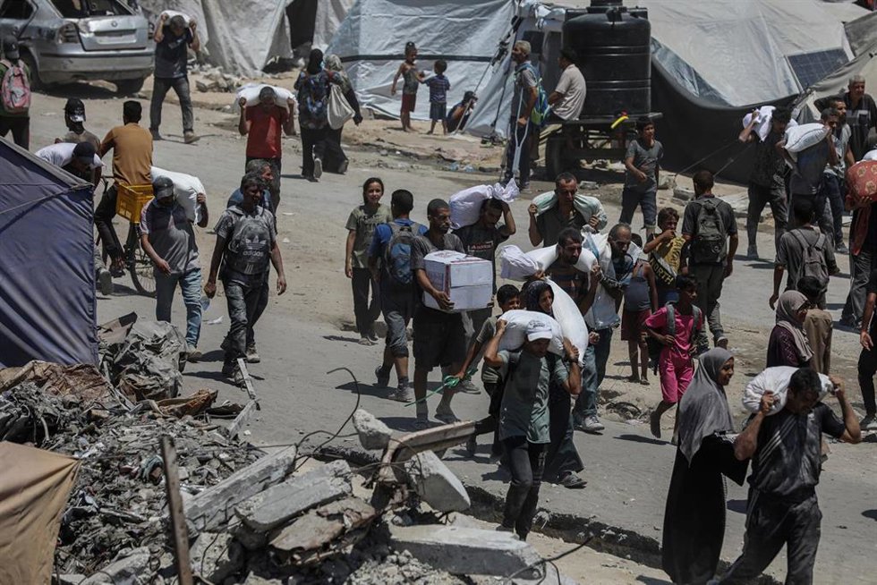 01 August 2025, Palestinian Territories, Jabalia: Palestinians carry sacks of flour they collected from a humanitarian aid convoy, as they make their way along a destroyed road in Jabalia.  Photo: Omar Ashtawy/APA Images via ZUMA Press Wire/dpa