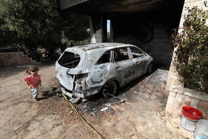 RAMALLAH, 1 de agosto de 2025 -- Uma menina palestina passa correndo por um carro queimado após um ataque de colonos israelenses no vilarejo de Silwad, na cidade de Ramallah, na Cisjordânia, em 31 de julho de 2025.