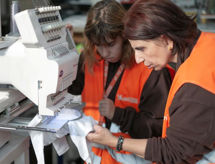 Dos personas de la Fundación Juan XXIII trabajan en la elaboración de una canastilla.
