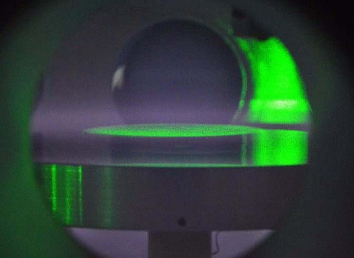 Una vista dentro de la cámara de vacío del laboratorio, donde las partículas coloidales están suspendidas en un disco plano, iluminado por la luz verde de un láser, para estudiar el plasma polvoriento.