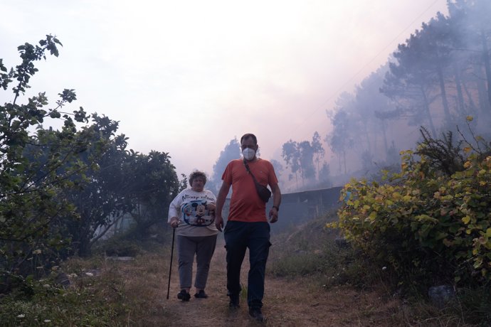 Dos personas huyen del fuego, a 5 de agosto de 2025, en Ponteceso, A Coruña, Galicia (España). Un nuevo incendio en el municipio coruñés de Ponteceso ha obligado este martes a desalojar a vecinos de la parroquia de Corme Aldea.