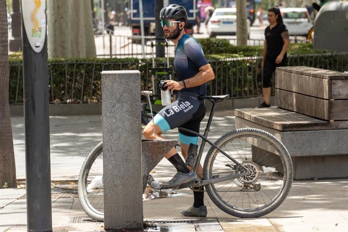 Archivo - Un ciclista llena una botella de una fuente de agua pública.