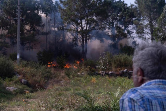 Una persona observa el fuego, a 5 de agosto de 2025, en Ponteceso, A Coruña, Galicia (España). Un nuevo incendio en el municipio coruñés de Ponteceso ha obligado este martes a desalojar a vecinos de la parroquia de Corme Aldea.