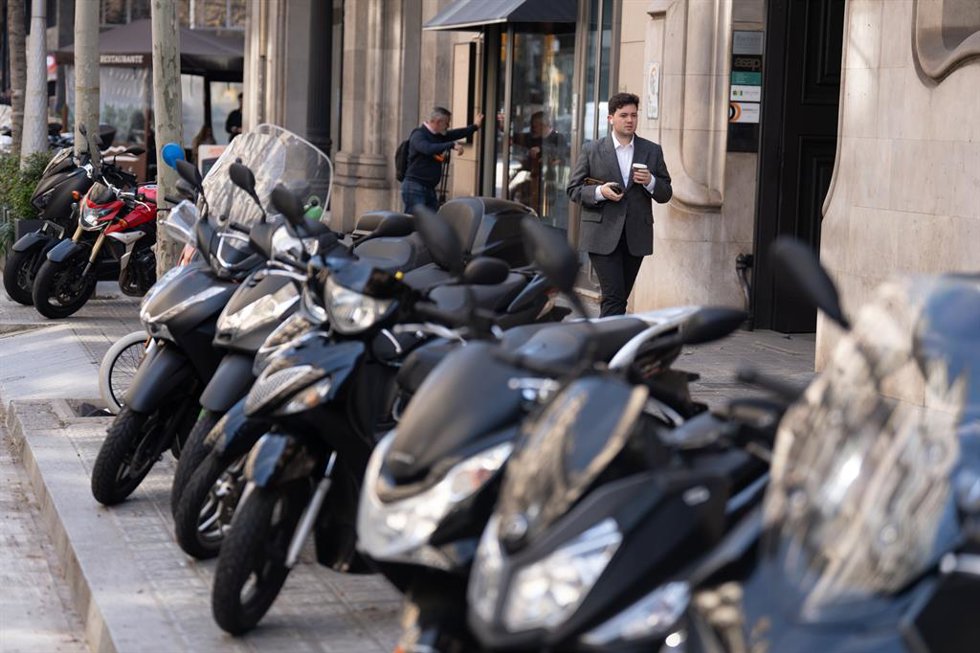 Archivo - Varias personas caminan al lado de motos aparcadas en la acera