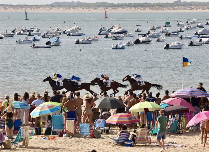 Bañistas asisten a las Carreras de Caballos de Sanlúcar, celebradas en la playa de la Pileta aprovechando la bajamar.
