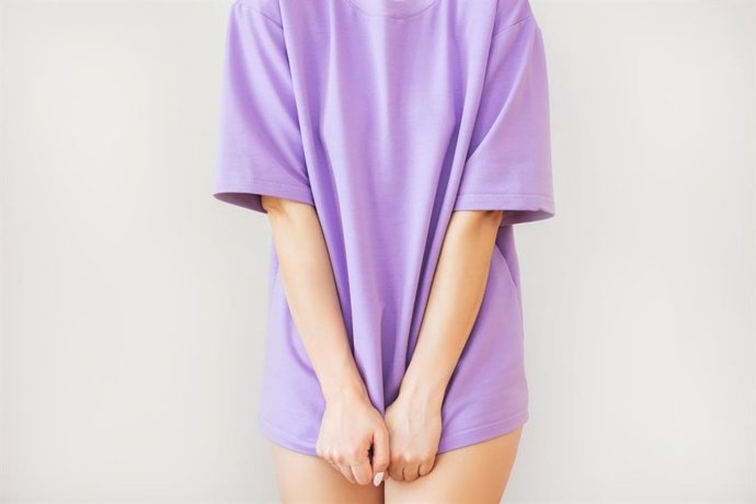 Archivo - Mujer parada en una camiseta púrpura y cubriendo su entrepierna con las manos, sufre de incontinencia urinaria, cistitis, vaginosis.