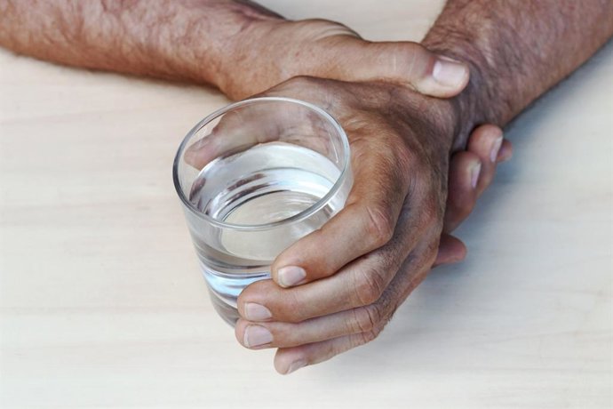 Archivo - Hombre se sujeta la mano que tiembla mientras sostiene un vaso.