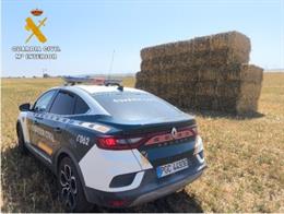 Un coche de la Guardia Civil delante de una pila de alpacas de forraje.