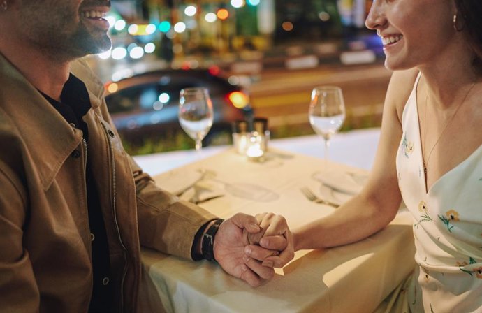 Archivo - Pareja joven sonriente tomados de la mano durante una cena por la noch