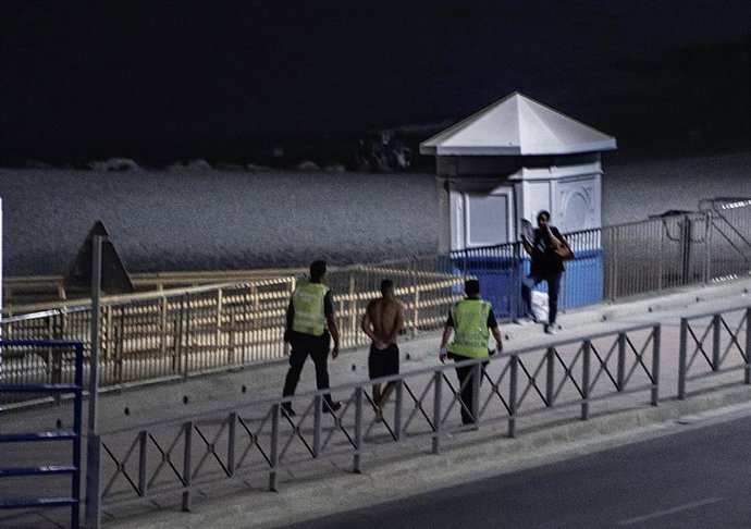 Archivo - Un migrante detenido por dos agentes de la Guardia Civil tras entrar a nado por la playa del Tarajal. Imagen de archivo. 