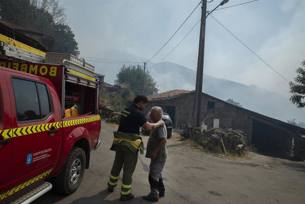 Un residente y un bombero después de la noche con el fuego alrededor de la aldea, a 10 de agosto de 2025, en Maceda, Ourense, Galicia (España). Un incendio en Maceda (Ourense), parroquia de Castro de Escuadro, calcina más de 20 hectáreas desde su inicio