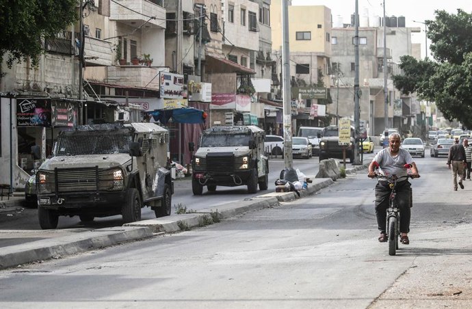 11 de agosto de 2025, Nablus, Cisjordânia, Palestina: Um homem palestino idoso é visto andando de bicicleta ao lado de veículos militares israelenses durante uma batida no campo de refugiados de Balata. A violência na cidade ocupada por Israel desde 1967 