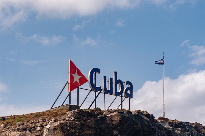 Archivo - Arquivo - 28 de março de 2025, Havana, Cuba: A bandeira tremula atrás da placa de Cuba em Havana. Havana, a capital de Cuba, é uma cidade de história rica, cultura vibrante e charme colonial. Conhecida por suas ruas coloridas, carros antigos e m