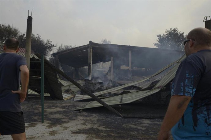 Dos ganaderos observan el estado de su granja tras el paso del fuego, a 13 de agosto de 2025, en Cova, Pobra de Trives, Ourense, Galicia (España).