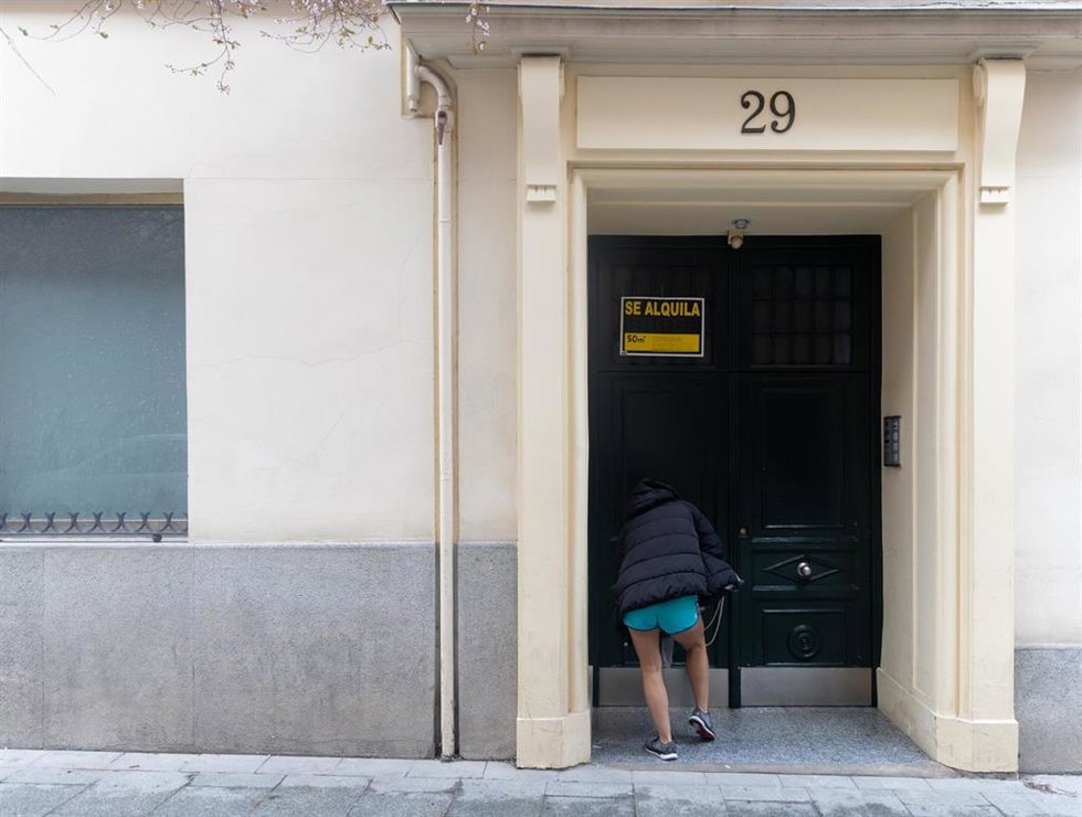 Archivo - Una persona pasa a un edificio donde hay un cartel de Se alquila.