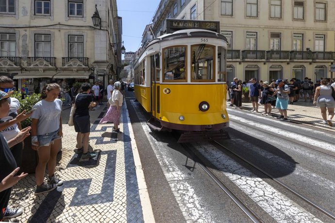 4 de agosto de 2025, Lisboa, Portugal: Pessoas caminham perto de um bonde que passa por uma das ruas do distrito de Baixa. Os verões portugueses são marcados por intensas ondas de calor, com temperaturas superiores a 35°C, afetando a vida cotidiana de mor