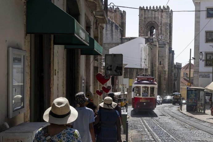 5 de agosto de 2025, Lisboa, Portugal: Pessoas caminham perto de um bonde que passa por uma das ruas do bairro da Graça, em Lisboa. Neste verão, Portugal está lidando com temperaturas realmente altas, com termômetros muito acima do normal e colocando as á