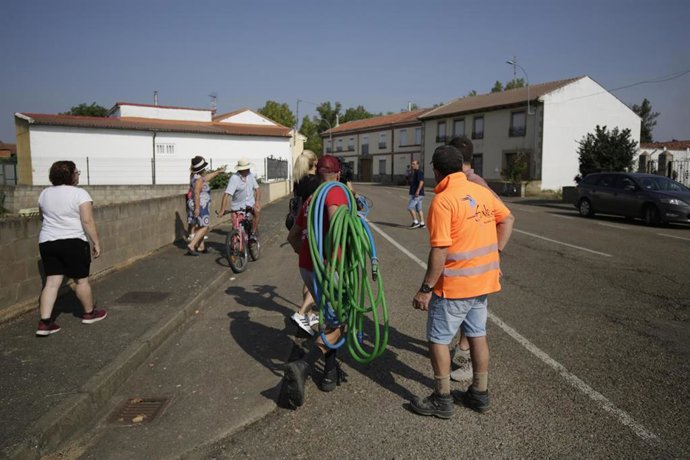 Vecinos caminan con mangueras a cuestas, a 14 de agosto de 2025, en  Villamontán de la Valduerna, León, Castilla y León (España). 