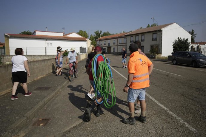 Moradores caminham com mangueiras nas costas, em 14 de agosto de 2025, em Villamontán de la Valduerna, León, Castilla y León (Espanha). Hoje, um segundo voluntário morreu, Jaime Aparicio, um dos sete feridos que permaneceu no hospital com 85% do corpo int