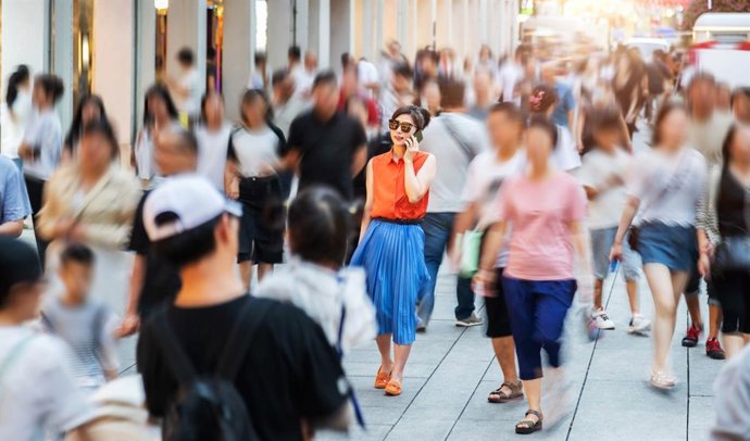 Archivo - Mujer de moda usando teléfono inteligente y caminando en calle concurrida