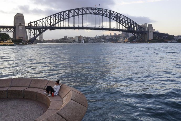 4 de agosto de 2025, Sydney, Estado de Nova Gales do Sul, Austrália: Uma mulher sentada com a Sydney Harbour Bridge visível ao fundo. Moradores e visitantes se reuniram na Sydney Opera House durante o pôr do sol, uma atividade diária popular que destaca a