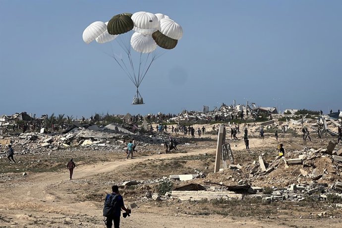 14 de agosto de 2025, Territórios Palestinos, Nuseirat: Palestinos correm para recuperar pacotes de ajuda lançados de paraquedas durante um lançamento aéreo sobre Nuseirat, na região central da Faixa de Gaza. Foto: Belal Abu Amer/APA Images via ZUMA Press