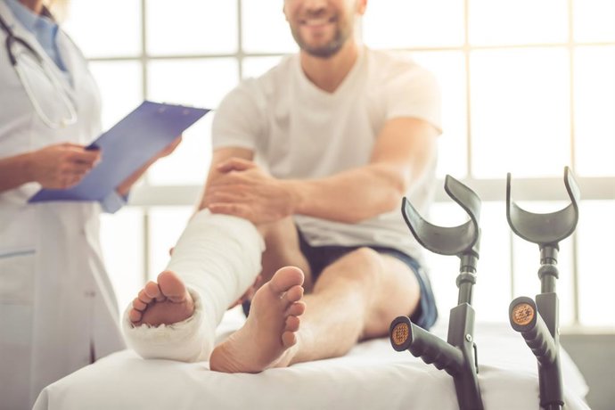 Archivo - Hombre con una pierna escayolada y muletas, en la consulta del médico.