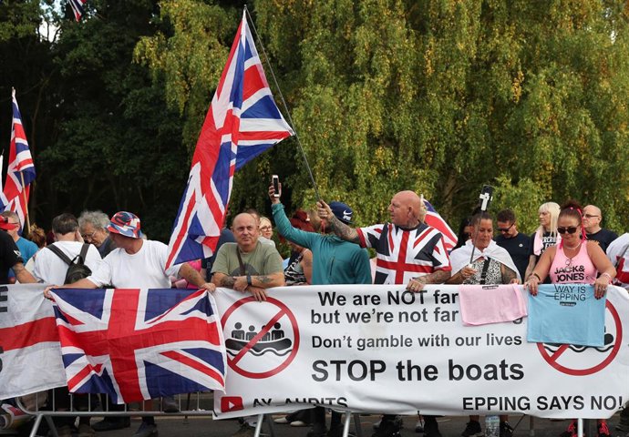 14 de agosto de 2025, Epping, Essex, Reino Unido: Epping, Reino Unido.  Manifestantes agitam bandeiras contra carros que passam, enquanto moradores locais realizam um protesto contra imigrantes do lado de fora do The Bell Hotel, em Epping. Um homem sírio 