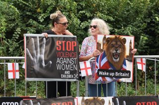 August 14, 2025, Epping, Essex, UK: Epping, UK. 2 Women hold placards up to passing cars, as local residents hold an anti-migrant protest outside The Bell Hotel, Epping. A Syrian man who is staying at the hotel, which houses asylum seekers, has appeared i