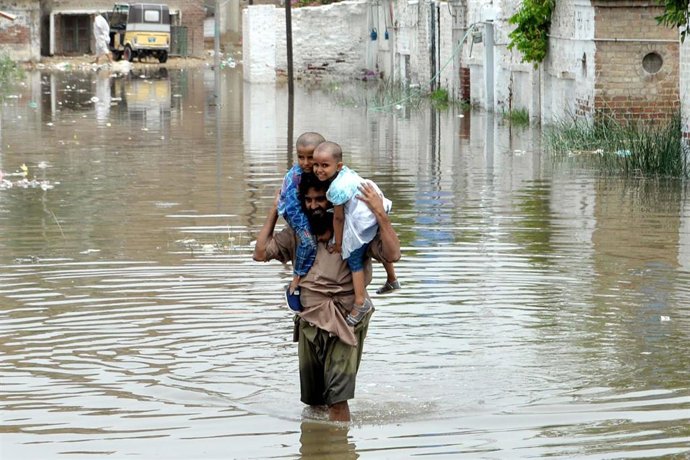 Archivo - Un hombre carga con dos niños durante las inundaciones de julio de este año en Pakistán.