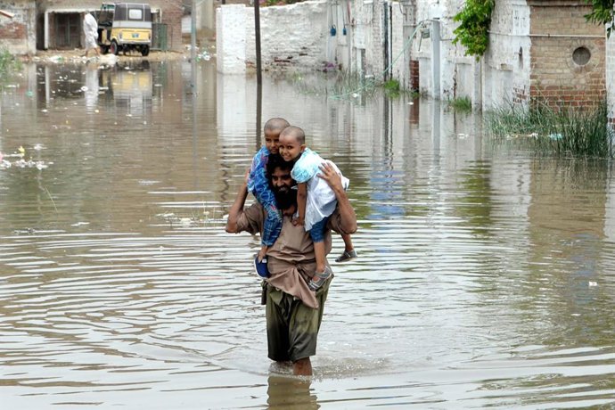 Archivo - HYDERABAD, July 16, 2025  -- A man carries his children as he wades through flood water after heavy monsoon rains in southern Pakistan's Hyderabad on July 15, 2025. Torrential monsoon rains and associated incidents have left at least 124 people 