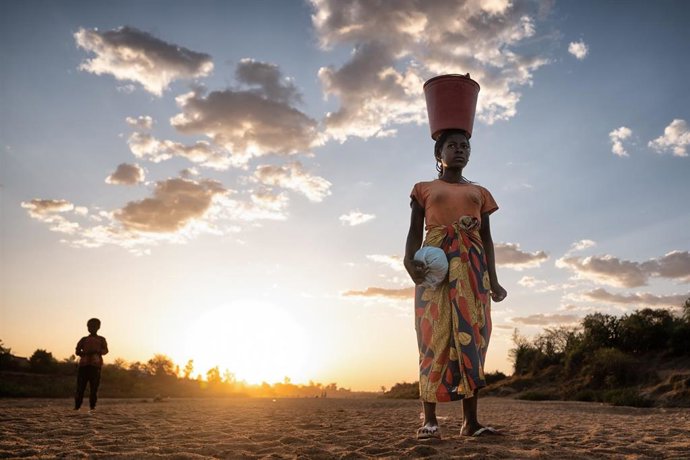 Archivo - Una mujer de pie en el lecho seco del río Menarandra (Madagascar), cargando un cubo rojo lleno de agua sobre la cabeza mientras regresa a casa.