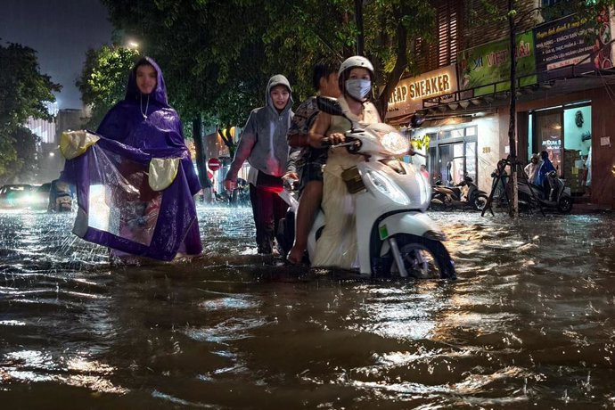 Archivo - Imagen de archivo de varias personas atravesando una calle anegada de Vietnam.