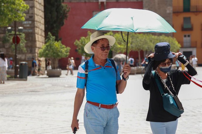 Archivo - Varios turistas se resguardan del sol con sombreros y paraguas para soportar las altas temperaturas en Sevilla. Foto de archivo. 