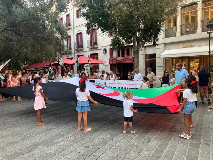 Niños saharauis del programa 'Vacances en Pau' y miembros de la Associació d'Amics del Poble Saharui de Baleares despliegan una gran bandera de la República Árabe Saharaui Democrática en la plaza de Cort.