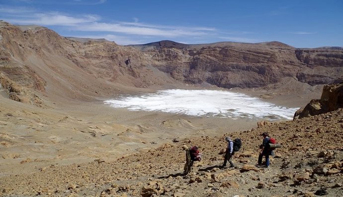 Descida na subcratera Era Kohor, dentro da caldeira do cume do Emi Koussi, a montanha mais alta do Saara, a 3415 m. Sedimentos esbranquiçados podem ser vistos no fundo da cratera: crostas de sal resultantes da secagem do lago.