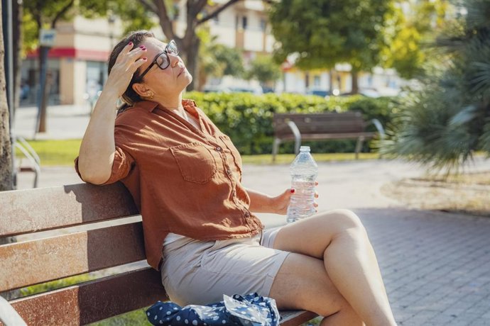 Archivo - Mujer con calor bebiendo agua sentada en un banco del parque.