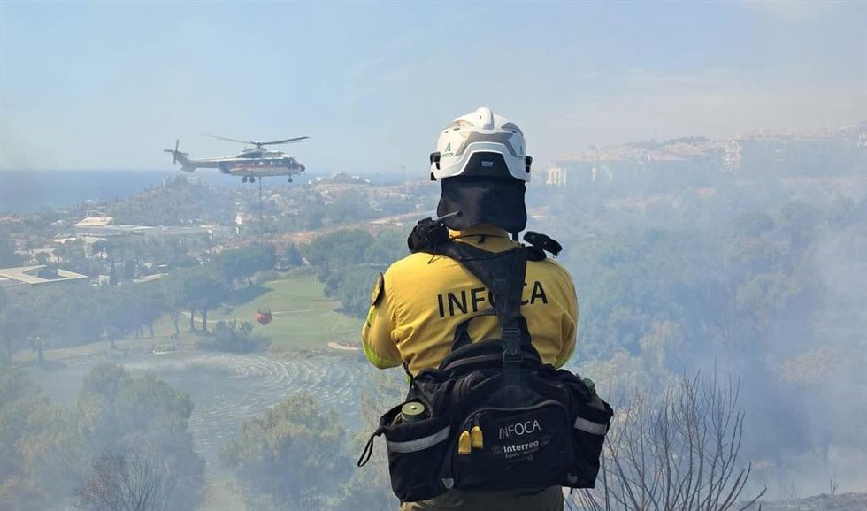 Un operario movilizado por el Plan Infoca contempla las tareas de un helicóptero en la extinción de un incendio en la zona de Santángelo Oeste en la ciudad malagueña de Benalmádena.
