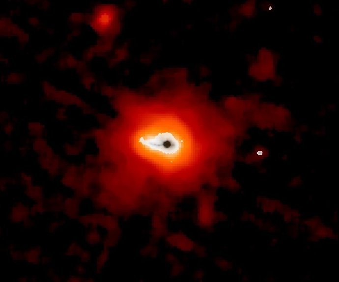 En el centro de esta imagen, la galaxia Makani se muestra en negro, rodeada por una emisión más tenue en blanco. Más allá, el polvo cálido en rojo, con las partículas más lejanas detectadas a una distancia de 114.000 años luz del centro de la galaxia