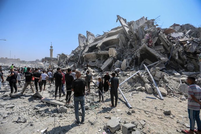 Un grup de persones al costat dels enderrocs d'una torre destruïda per un atac a la Franja de Gaza