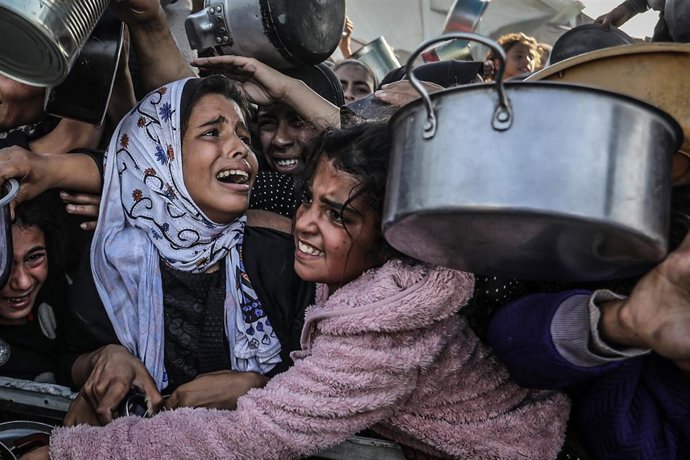 Archivo - Un grupo de niños palestinos desplazados espera para recibir alimentos en Gaza.